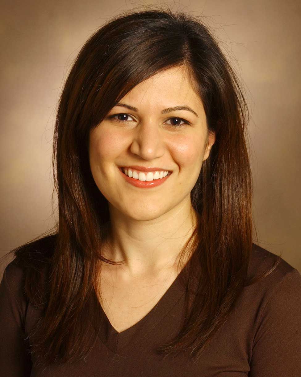 Smiling woman with dark hair in a brown top against a neutral studio background