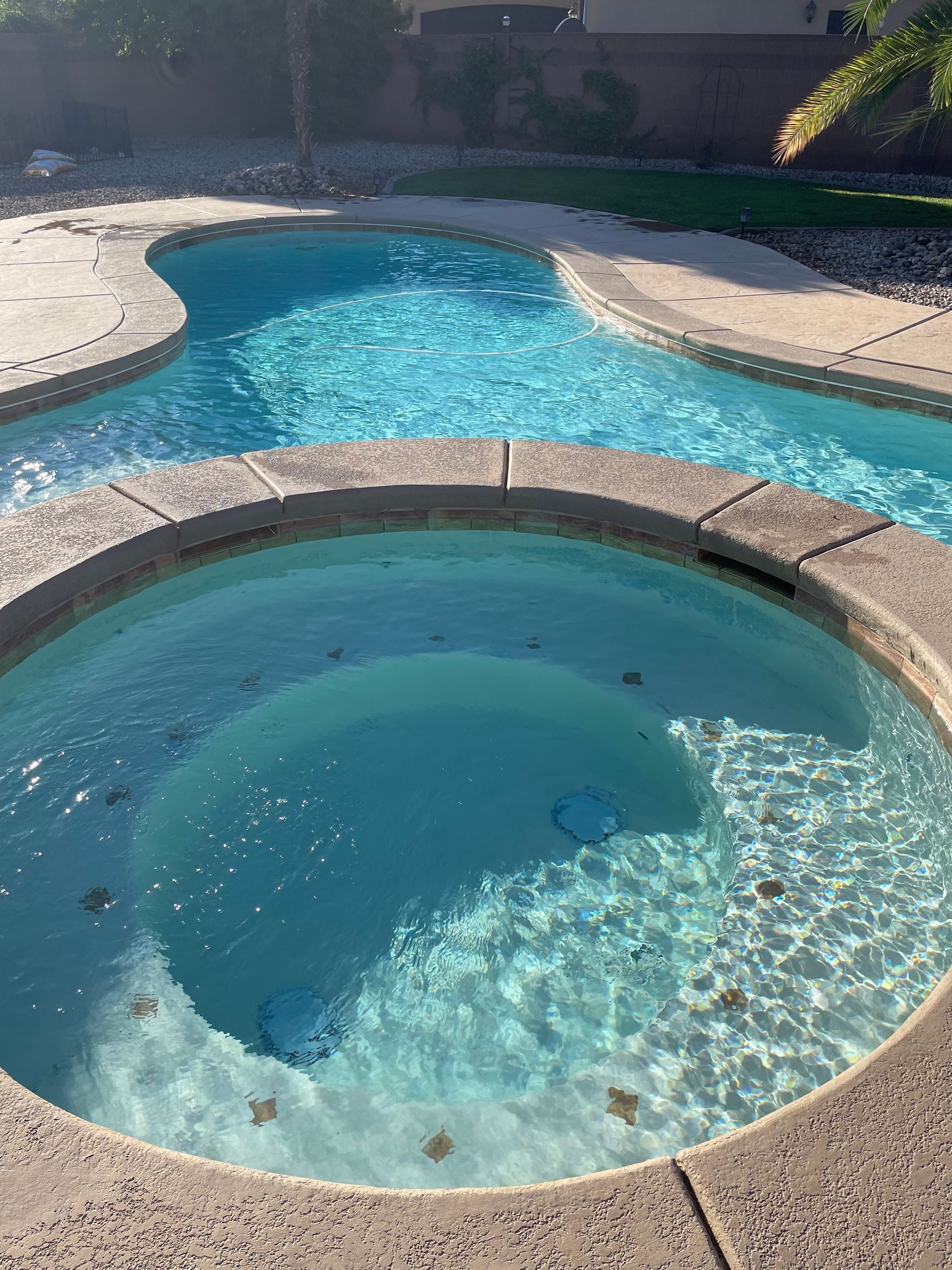 Swimming pool with a round hot tub in the foreground and a curved blue pool in the background.