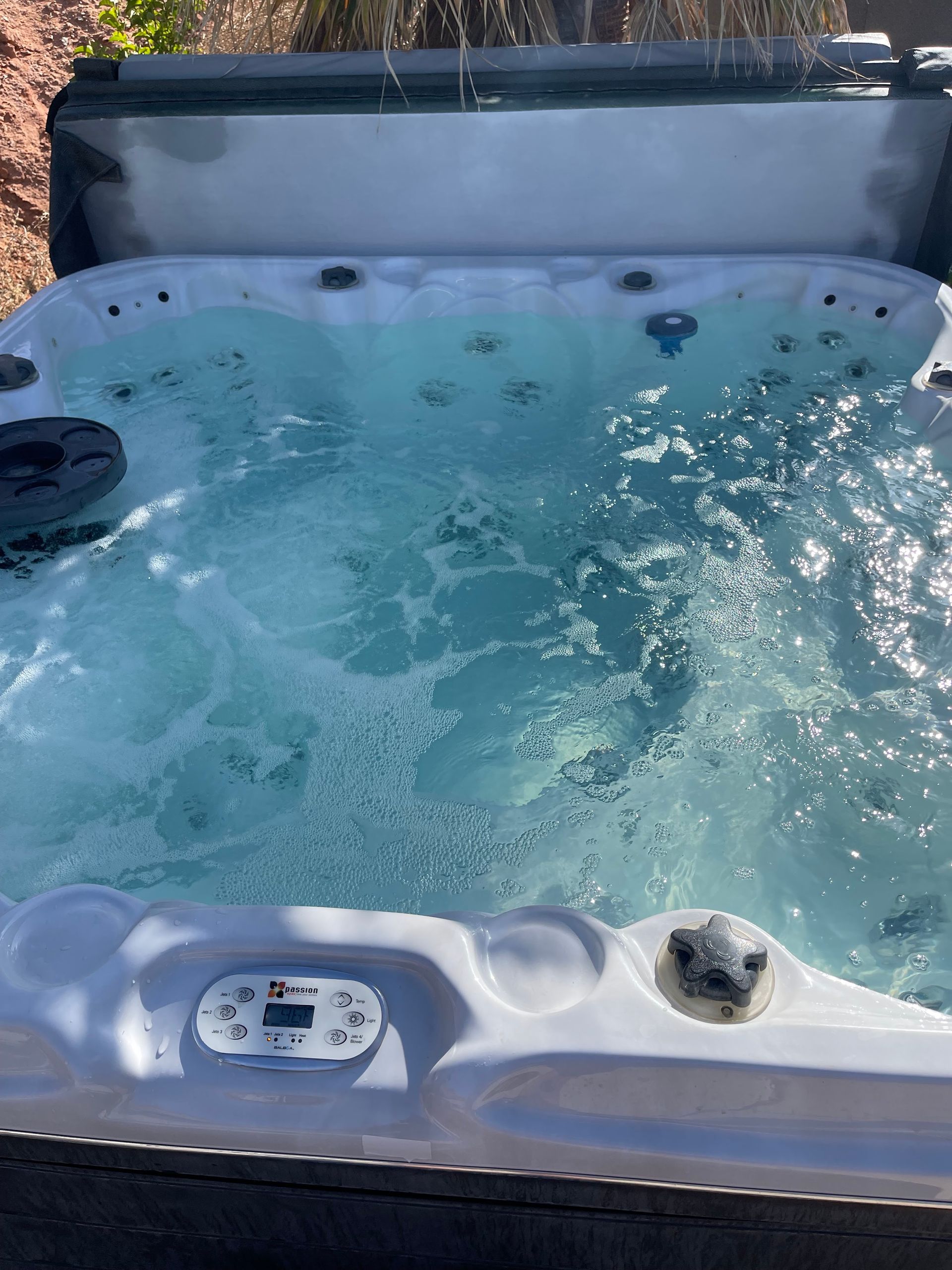 Outdoor hot tub with bubbling blue water and a gray cover in the background