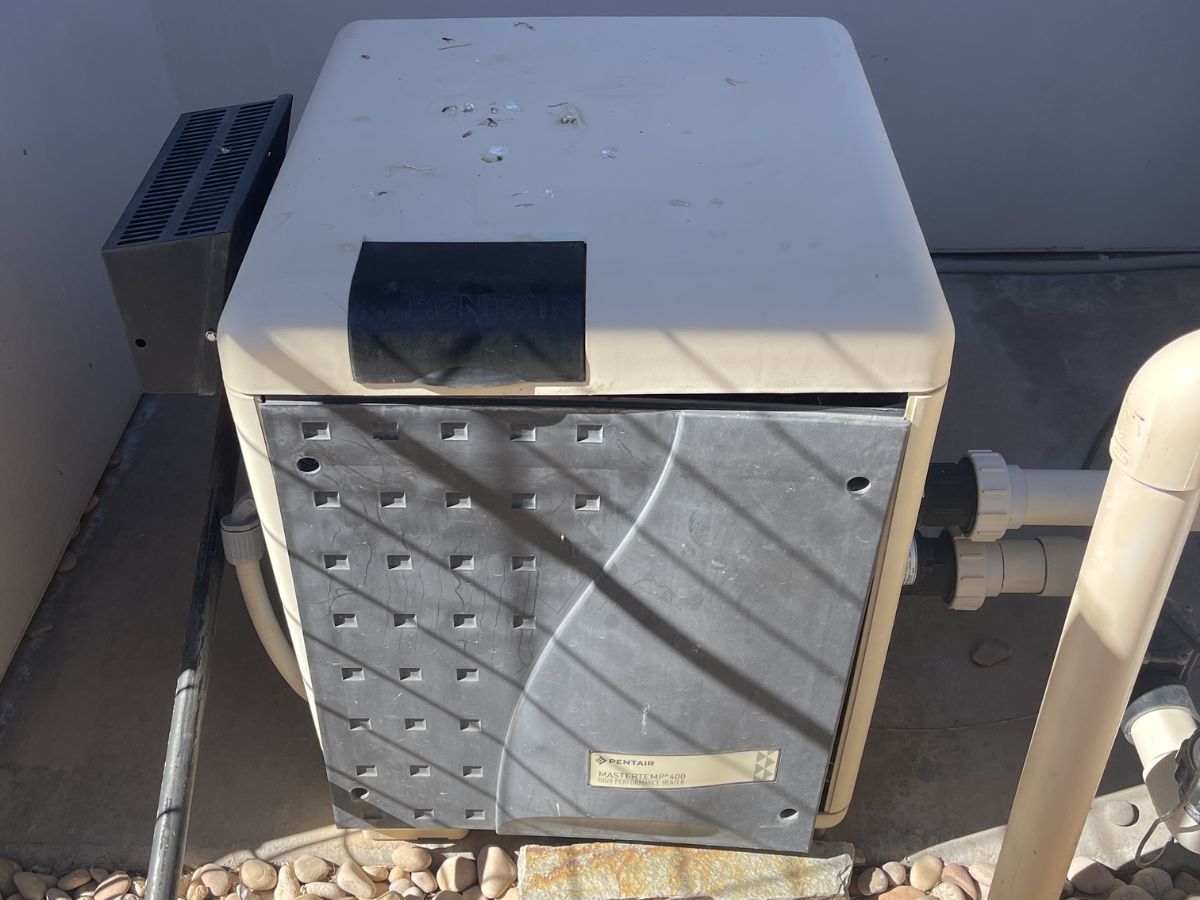 Outdoor HVAC unit beside a wall, with sunlight casting shadows across the front grille.