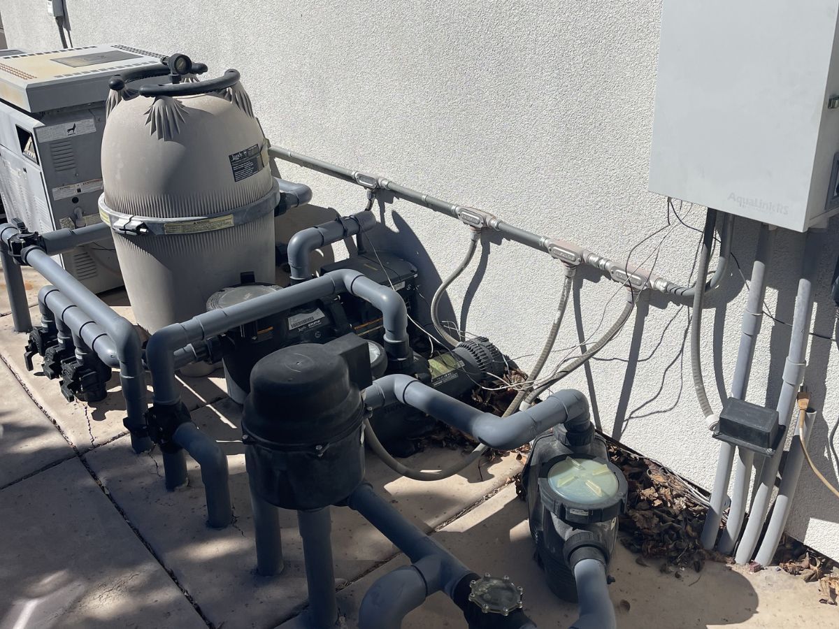 Rooftop HVAC equipment with pipes, valves, and electrical conduits along a wall