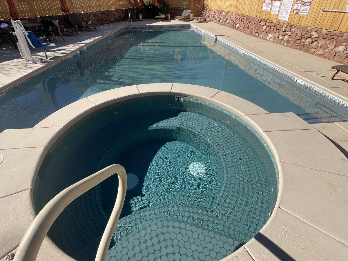 Outdoor pool with a circular hot tub and clear blue water beside tan tile decking