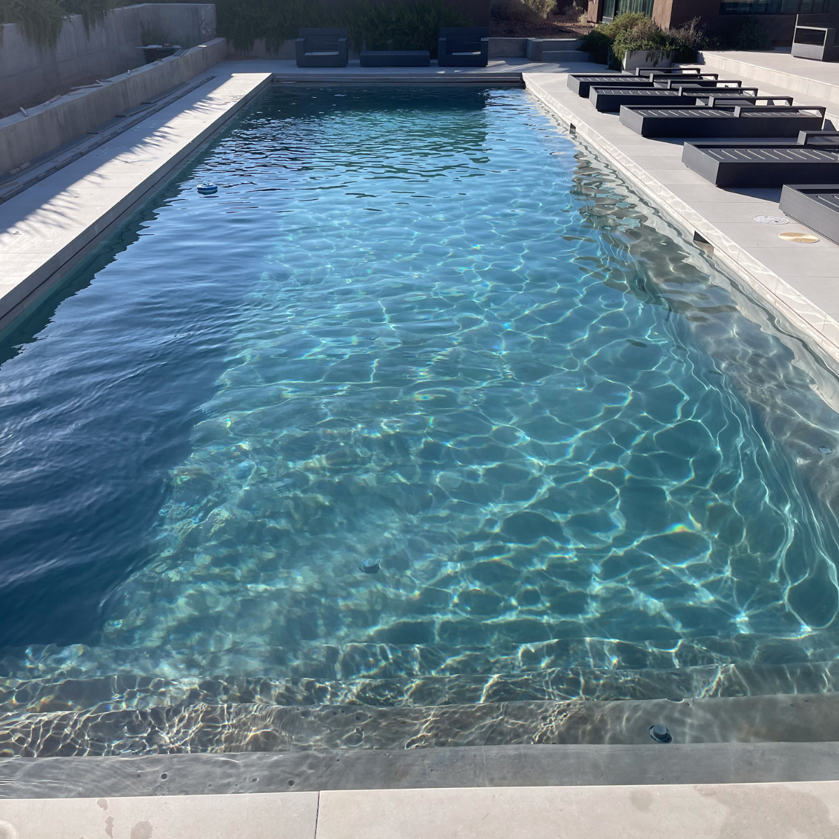 Rectangular outdoor swimming pool with clear blue water and lounge chairs along the right side