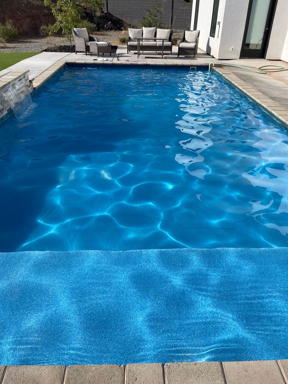 Blue swimming pool with sunlit ripples and lounge chairs in the background