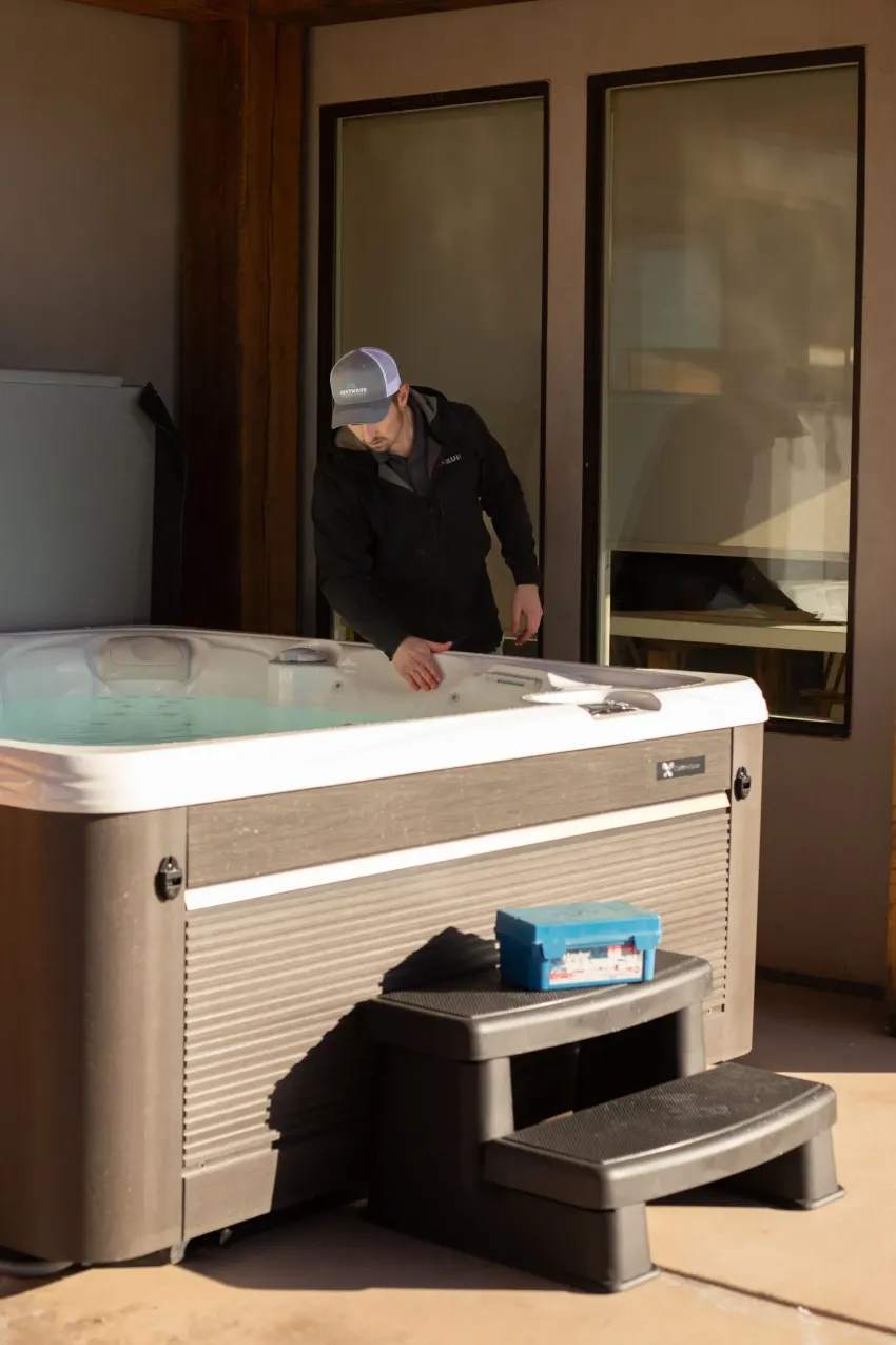 Man checking a hot tub on a patio beside a house with sliding glass doors