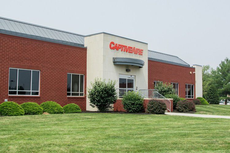 A one-story brick building with a white entrance featuring the red CaptiveAire logo, surrounded by green landscaping.