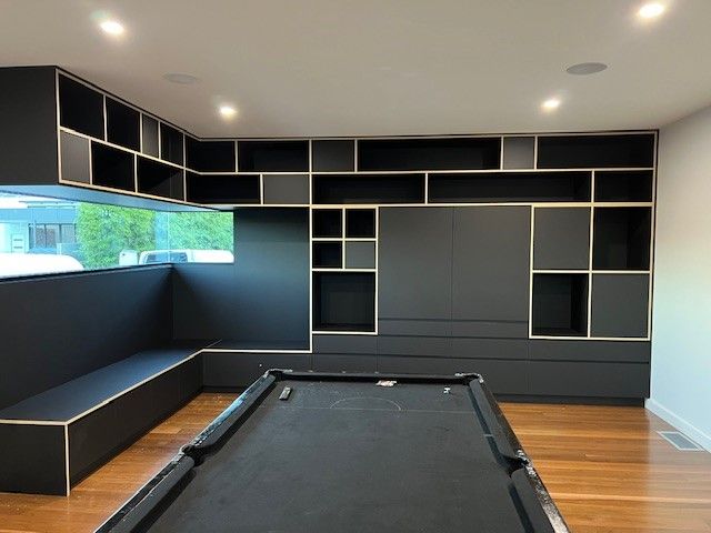 Modern game room with a pool table, built-in black and gray shelving, and a window seat.