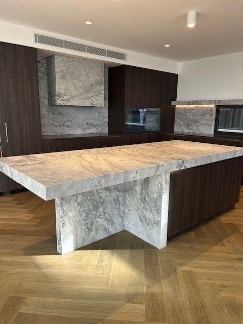 Kitchen with dark wood cabinets, a marble island and backsplash, and light wood herringbone floors.