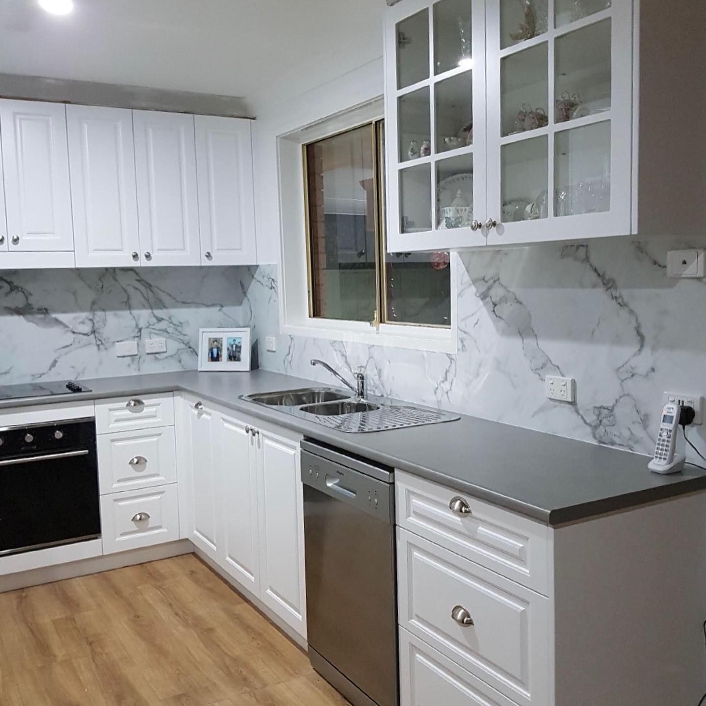 A Kitchen with White Cabinets, a Stainless Steel Dishwasher, a Sink, and A Window — Inovative Interiors In Maitland, NSW