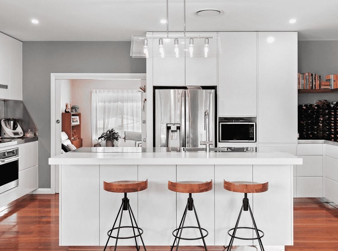 A Kitchen with White Cabinets Stools , a Refrigerator and A Sink — Inovative Interiors In Cardiff, NSW