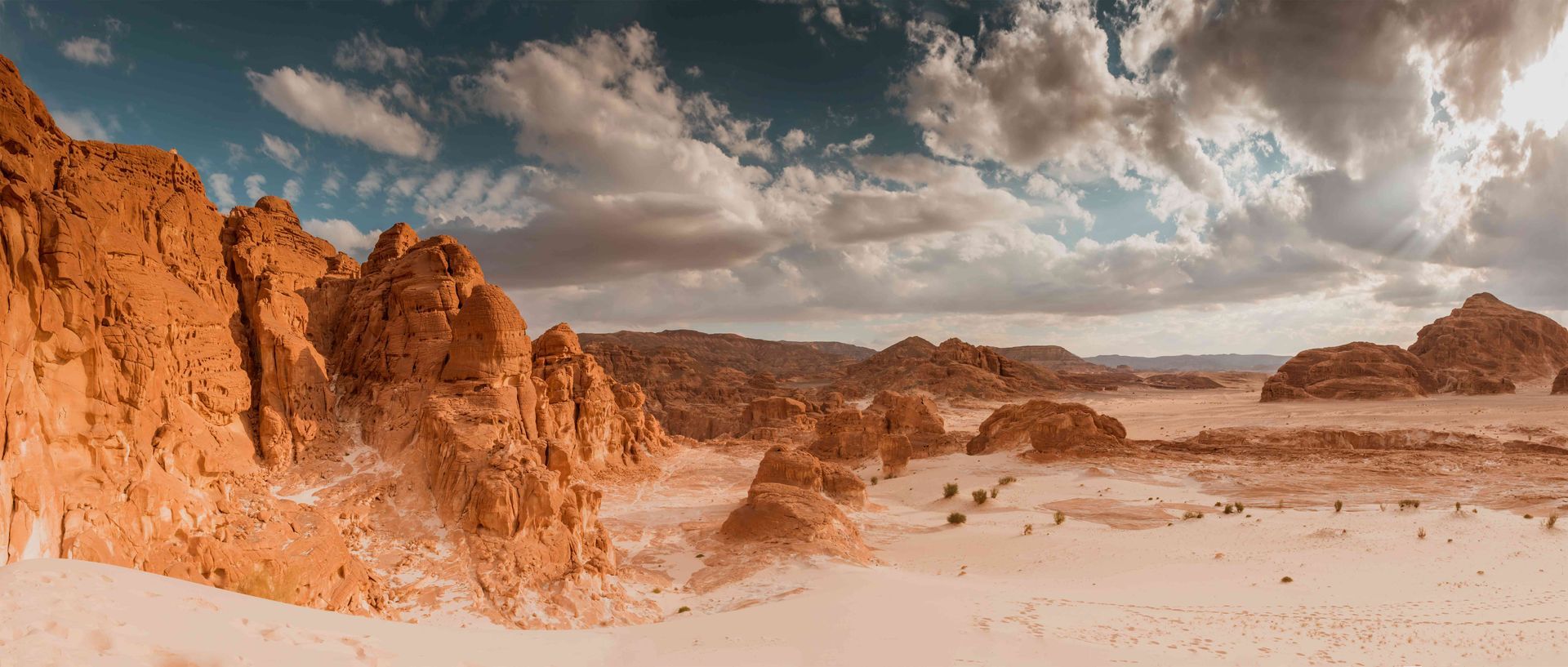 Sunlit desert cliffs and rocky dunes under a cloudy sky