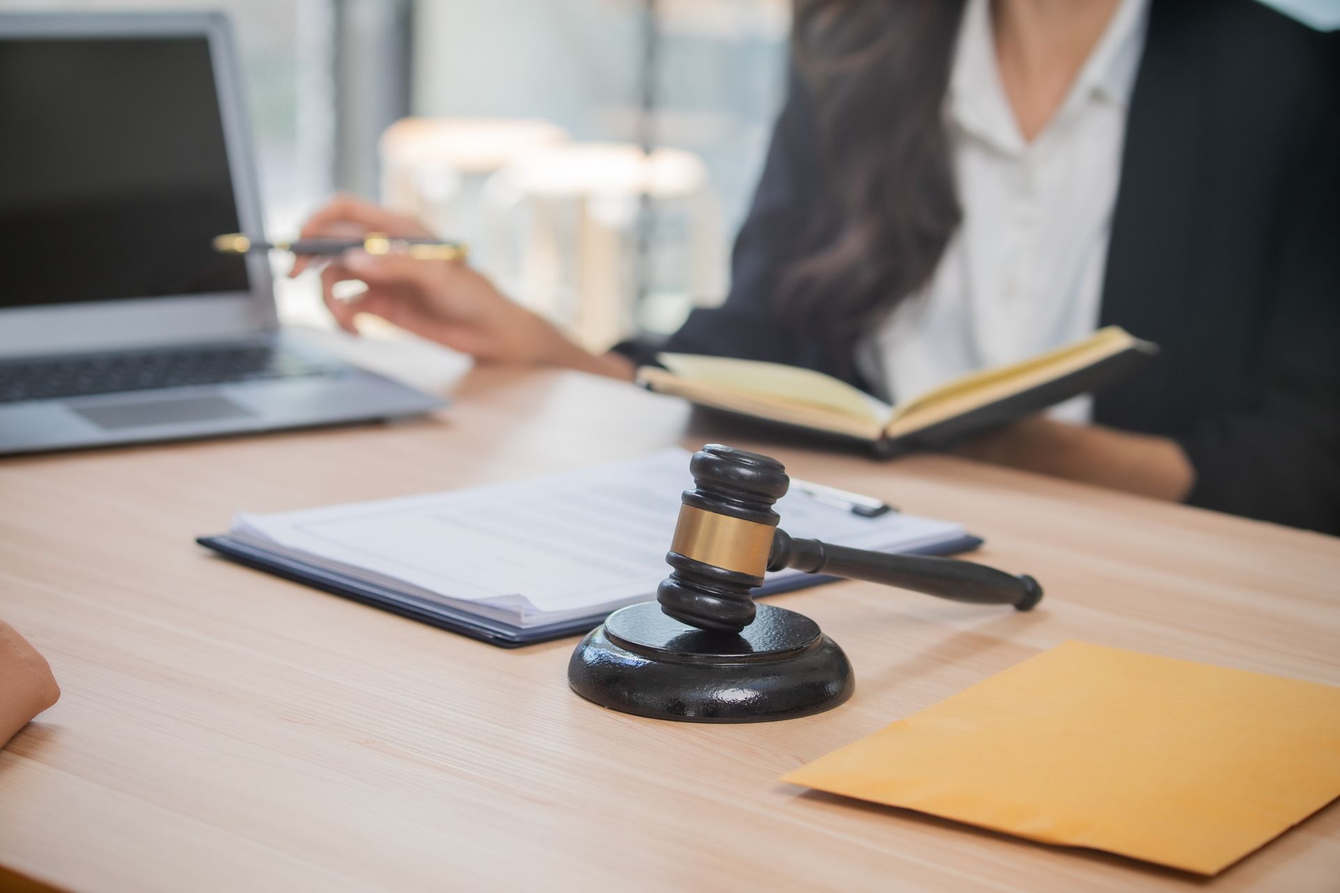 Lawyer’s desk with gavel, notebook, laptop, and a person taking notes in the background