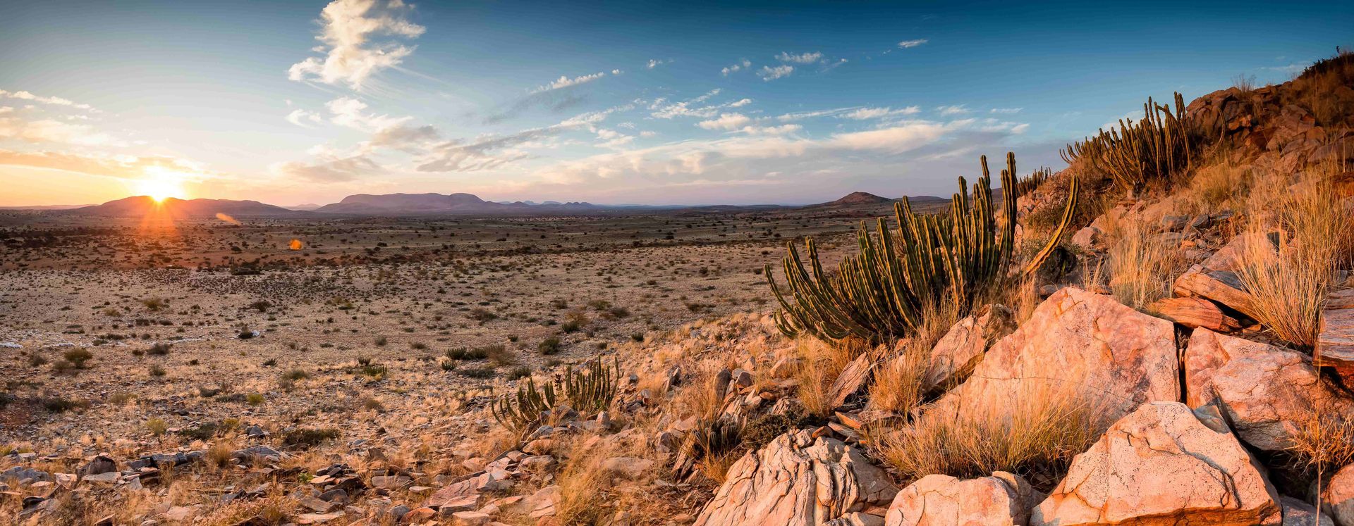 Sunset over a rocky desert landscape with sparse shrubs and distant mountains