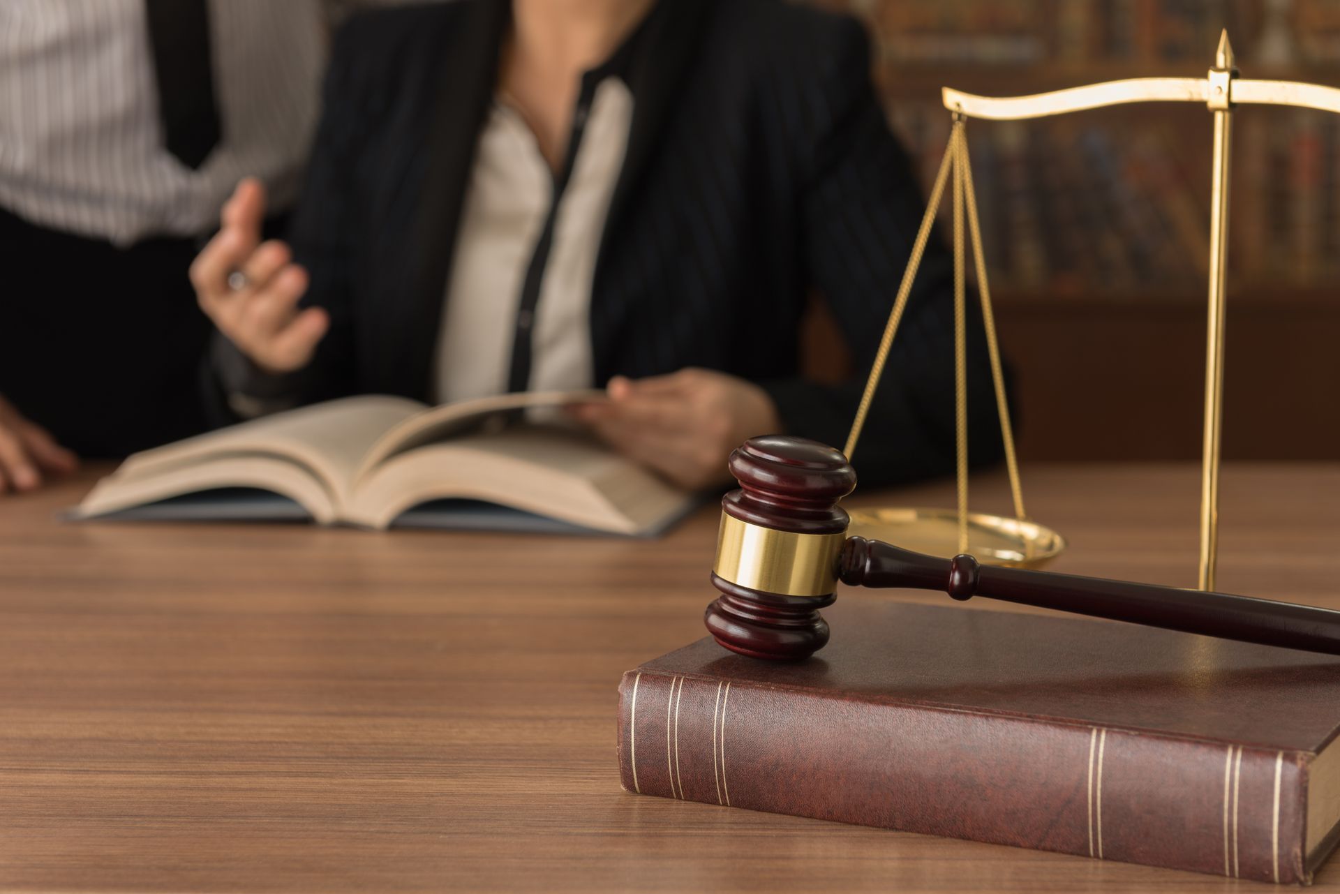 Law books and gavel on desk with scales, as a person reads in the background