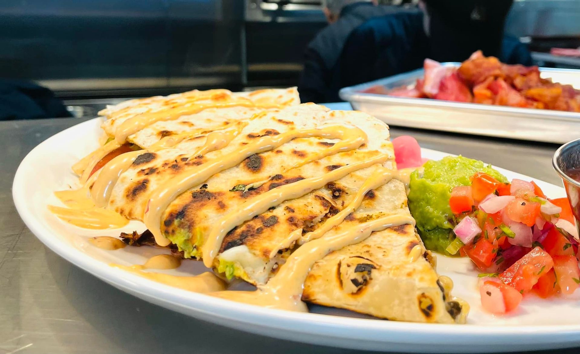 Plate of grilled stuffed crepes drizzled with sauce, served with fresh diced tomato salsa and sauce on the side