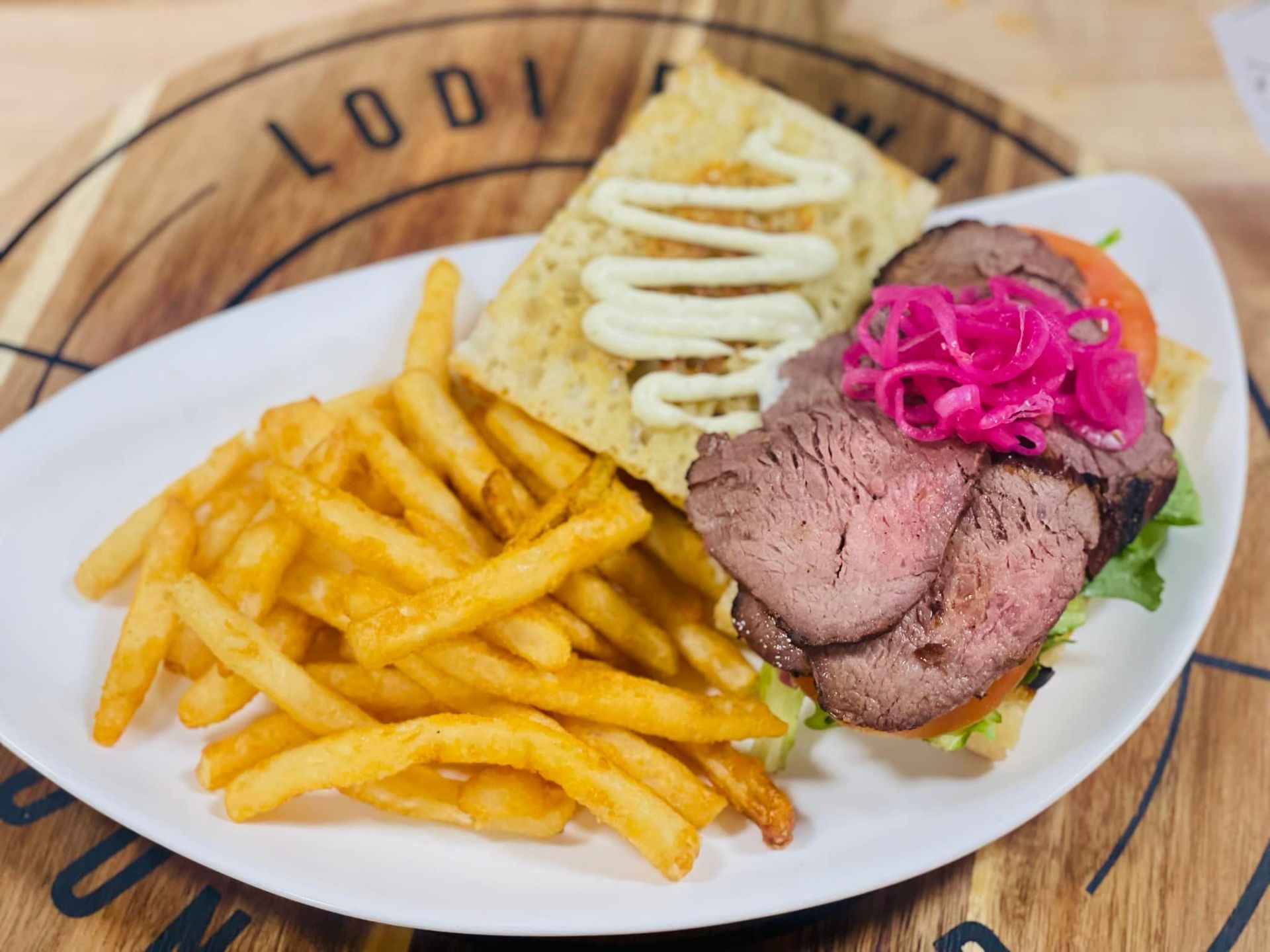 Plated fries with sliced steak, mashed potatoes, and pink garnish on a wooden table