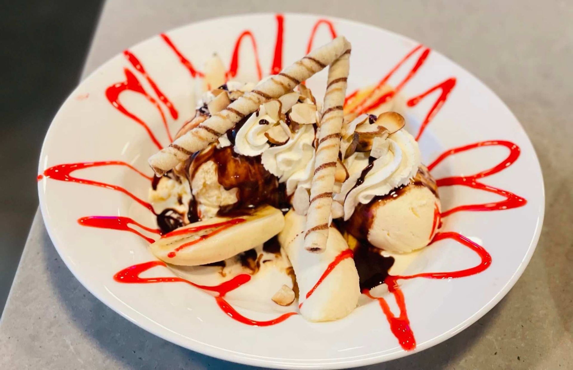Dessert plate with banana slices, whipped cream, chocolate drizzle, and red sauce on white dish