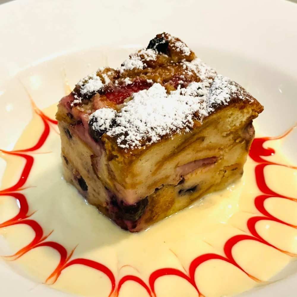 Dessert cube dusted with powdered sugar on a white plate, drizzled with red sauce