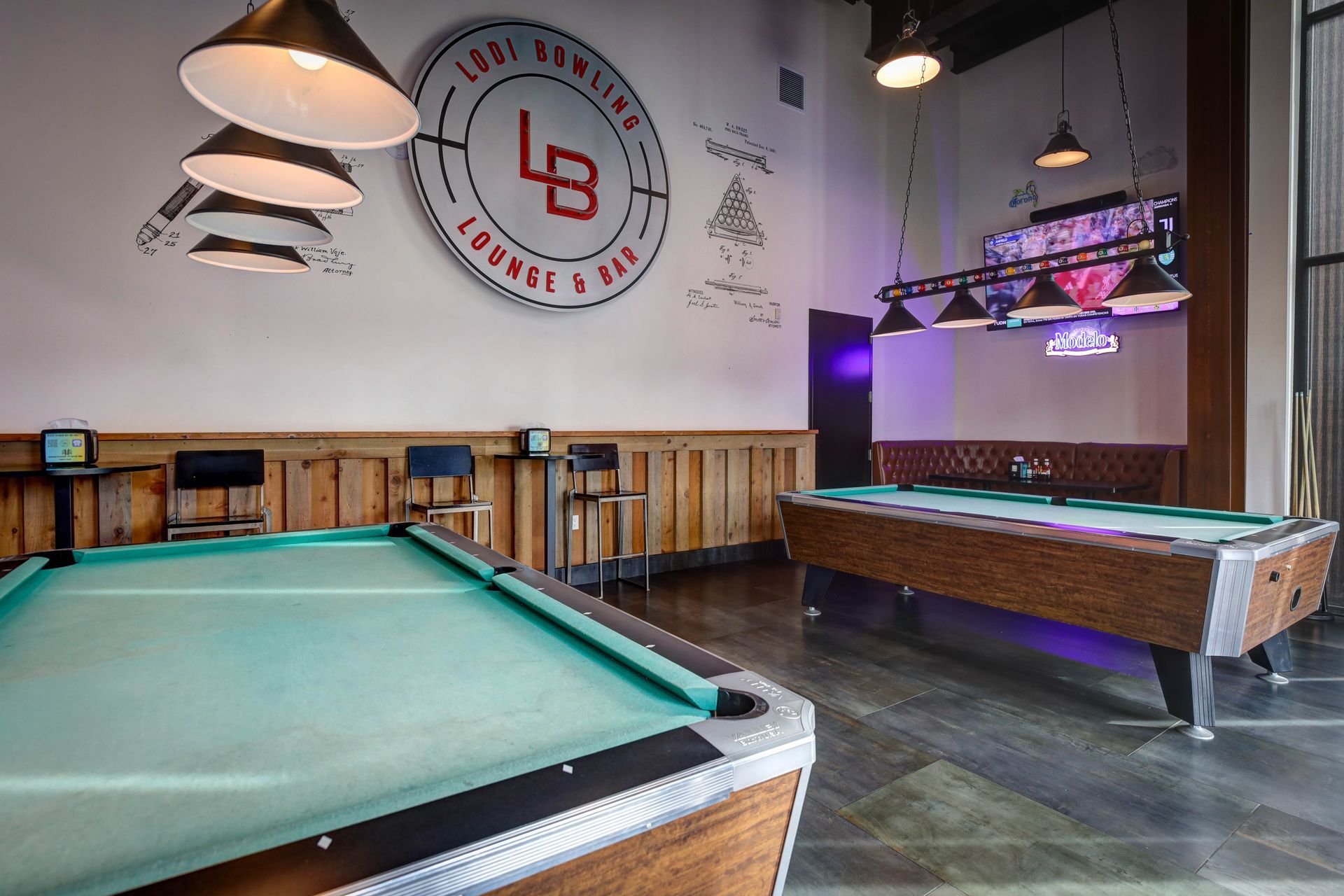 Game room with pool tables, pendant lights, wall logo, and a projector screen in the back.