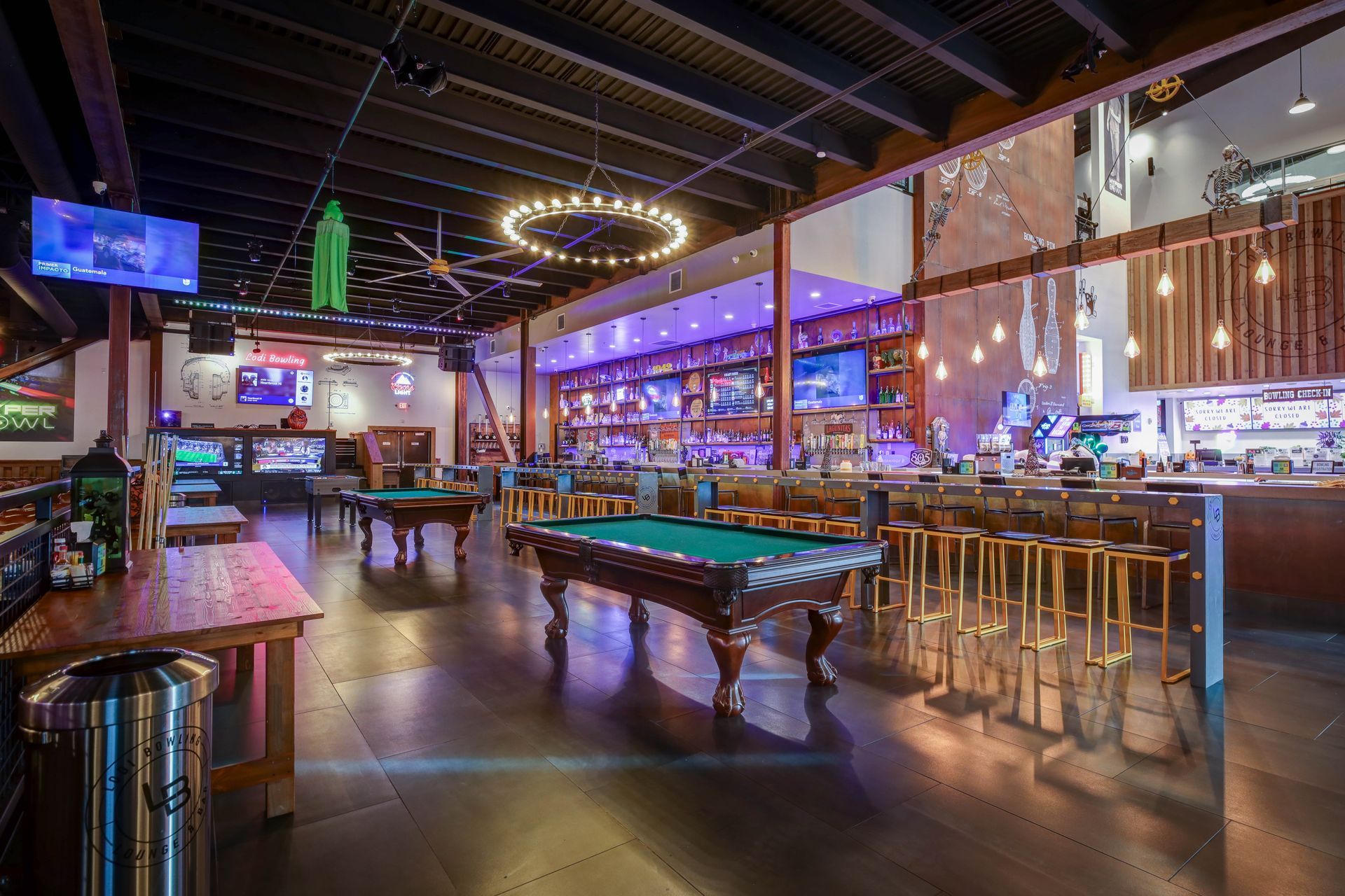 Neon-lit bar and billiards hall with pool tables, stools, and colorful ambient lighting