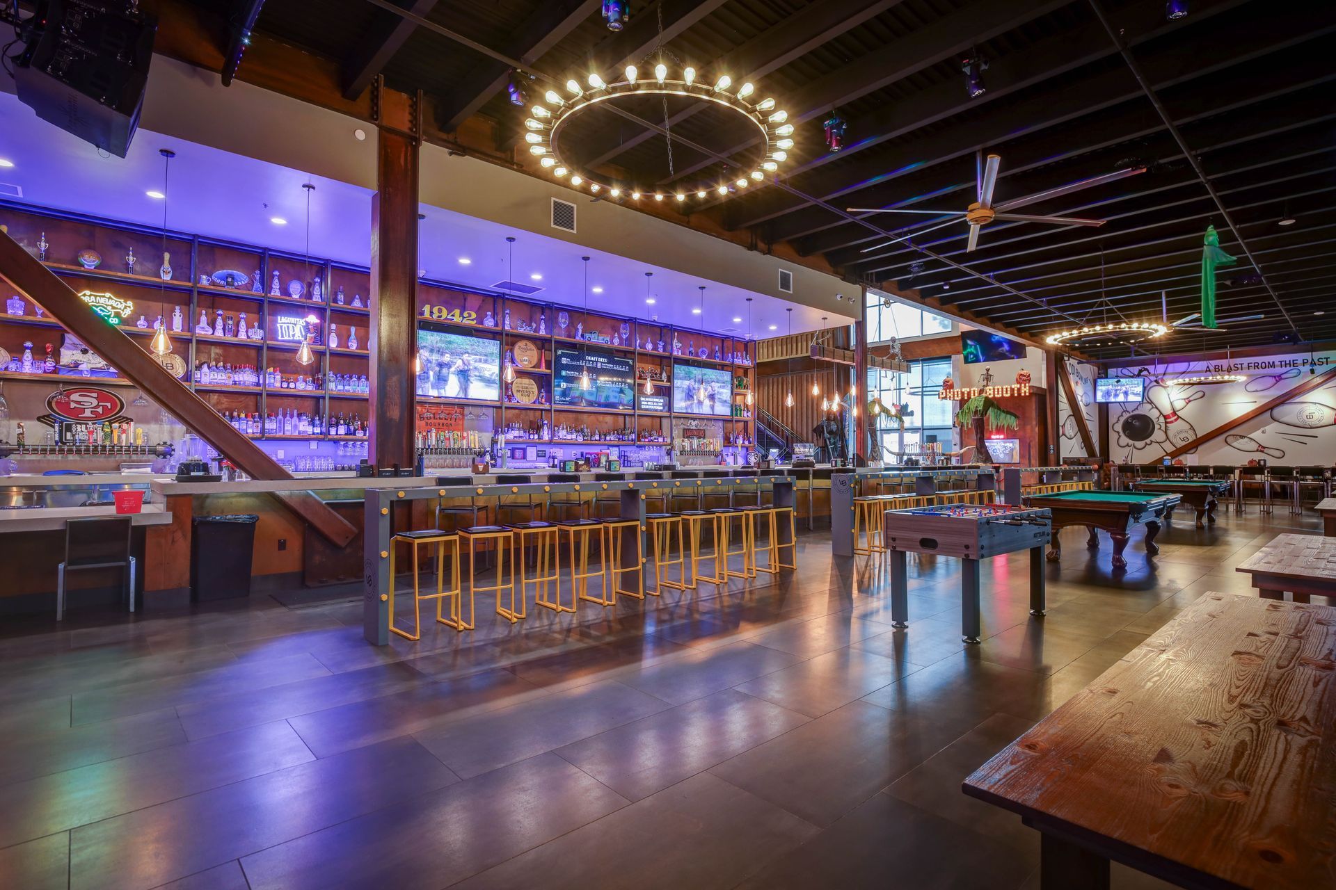 Modern bar interior with neon-lit backbar, circular ceiling lights, and polished wood tables