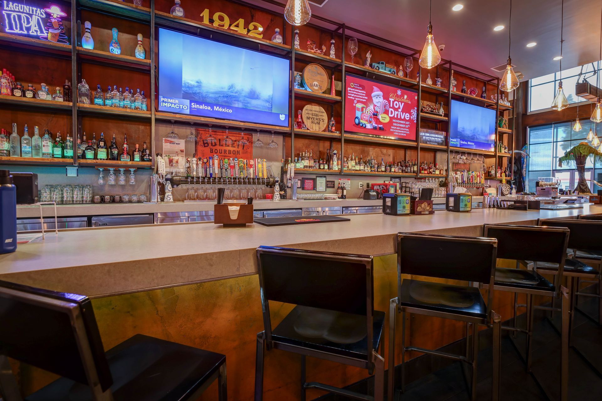 Empty sports bar interior with wooden bar, stools, and multiple TVs above the counter