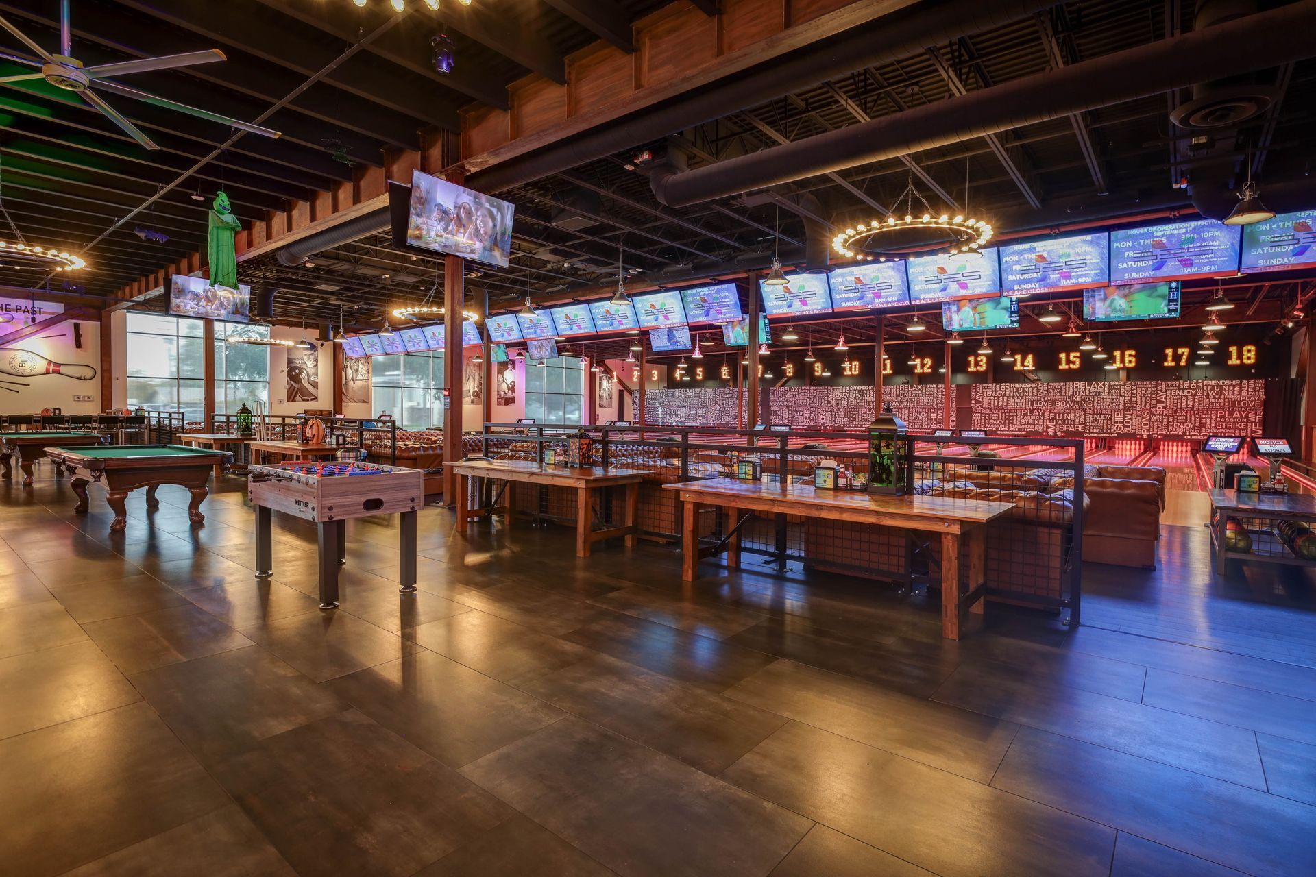 Dimly lit indoor food hall with long communal tables, colorful neon signs, and polished concrete floors