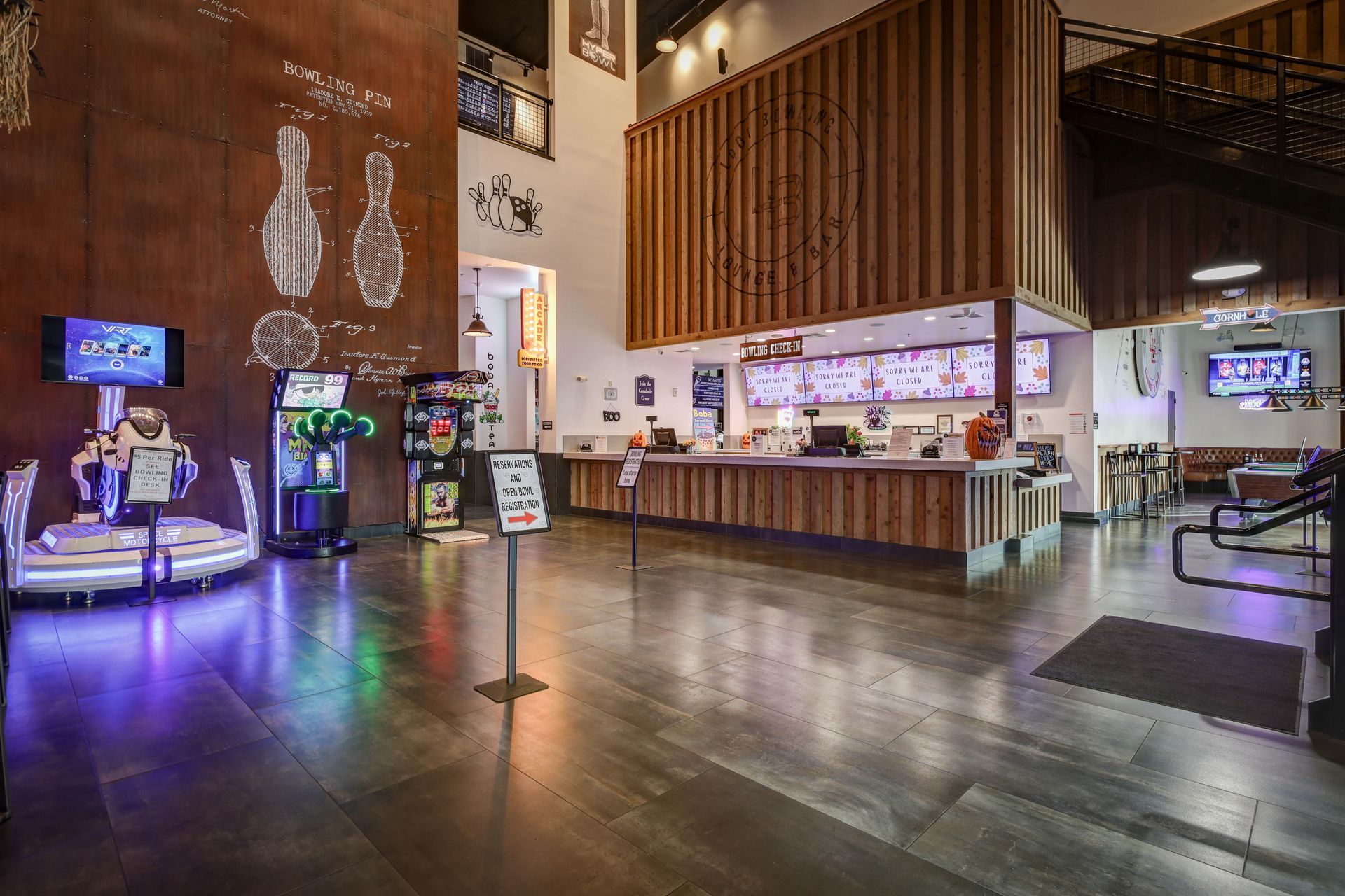 Modern lobby with polished floors, bar counter, hanging lights, and colorful arcade/game machines