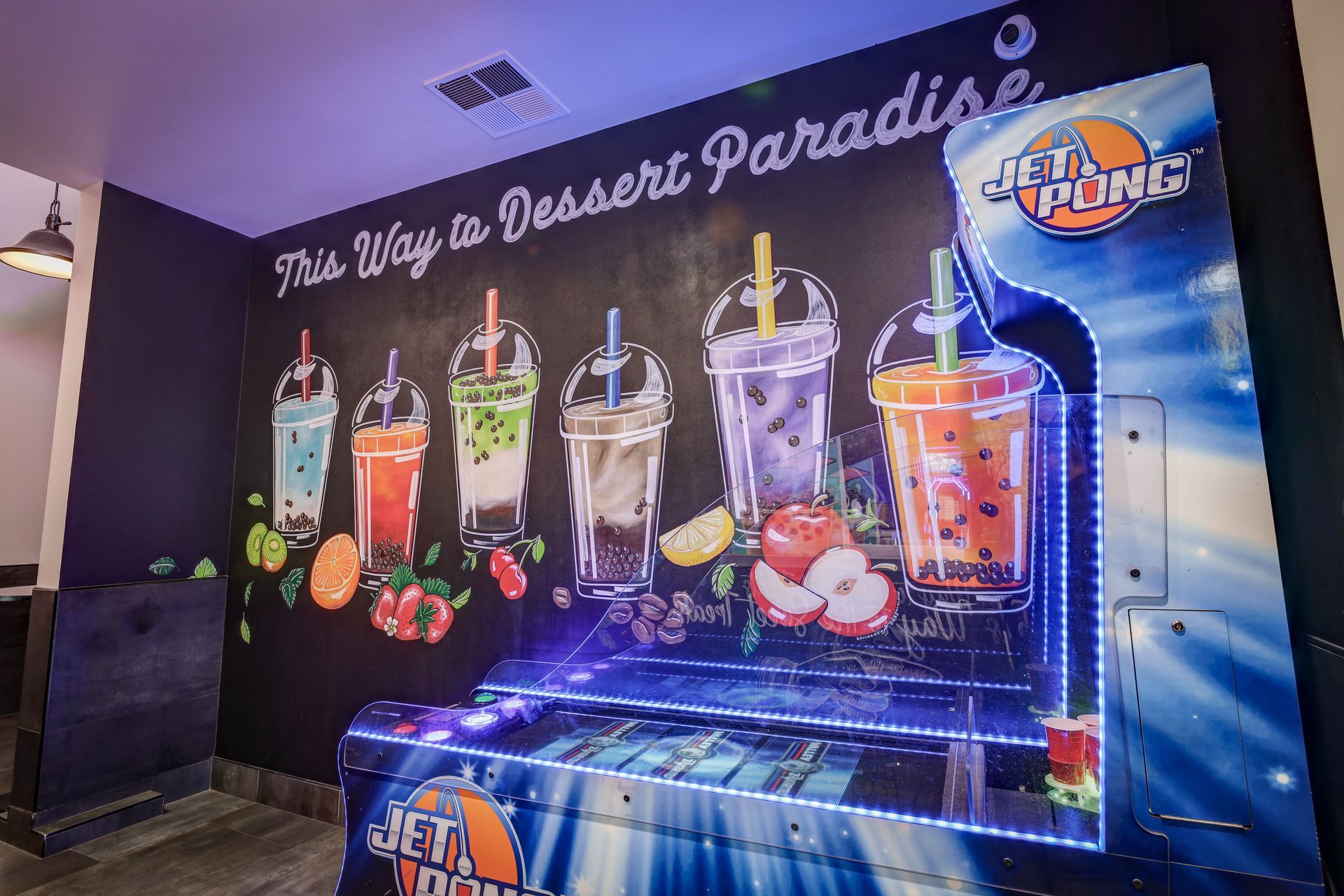 Black wall mural of colorful desserts and drinks with the phrase “This Way to Dessert Paradise” and a logo.