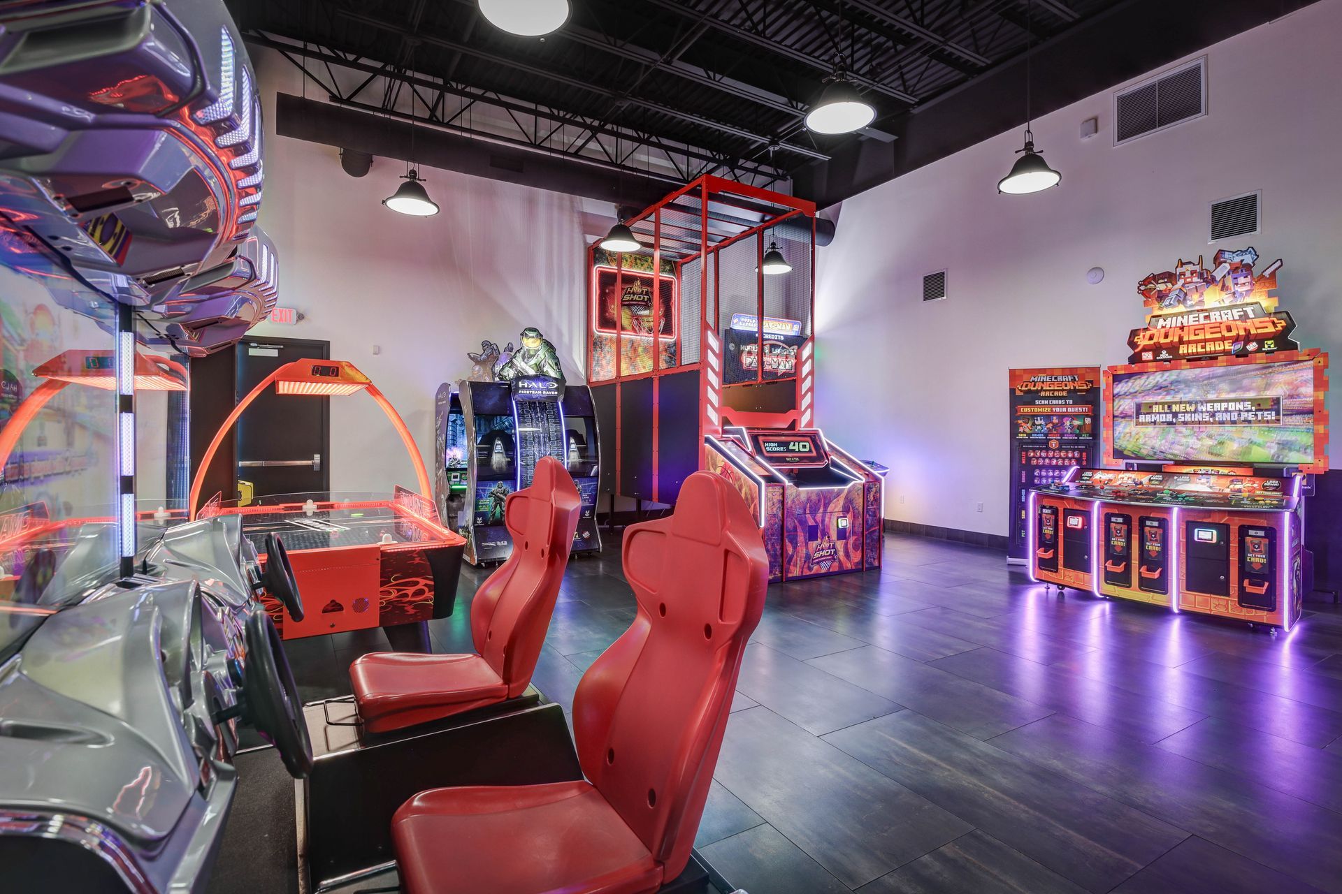 Empty arcade room with glowing game cabinets, red seats, and purple-lit floor