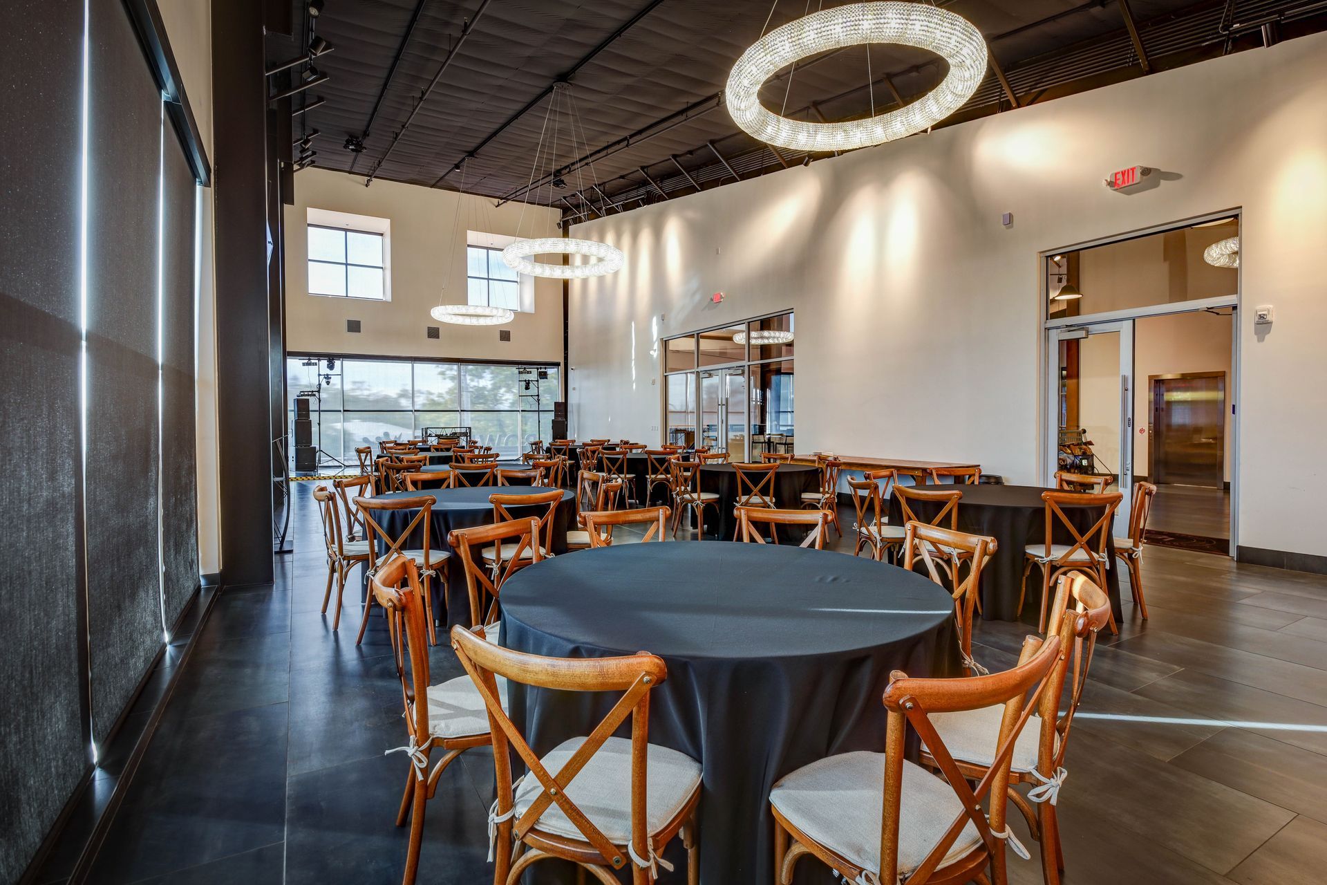 Empty restaurant dining room with wooden chairs, round tables, and modern ring lights near large windows