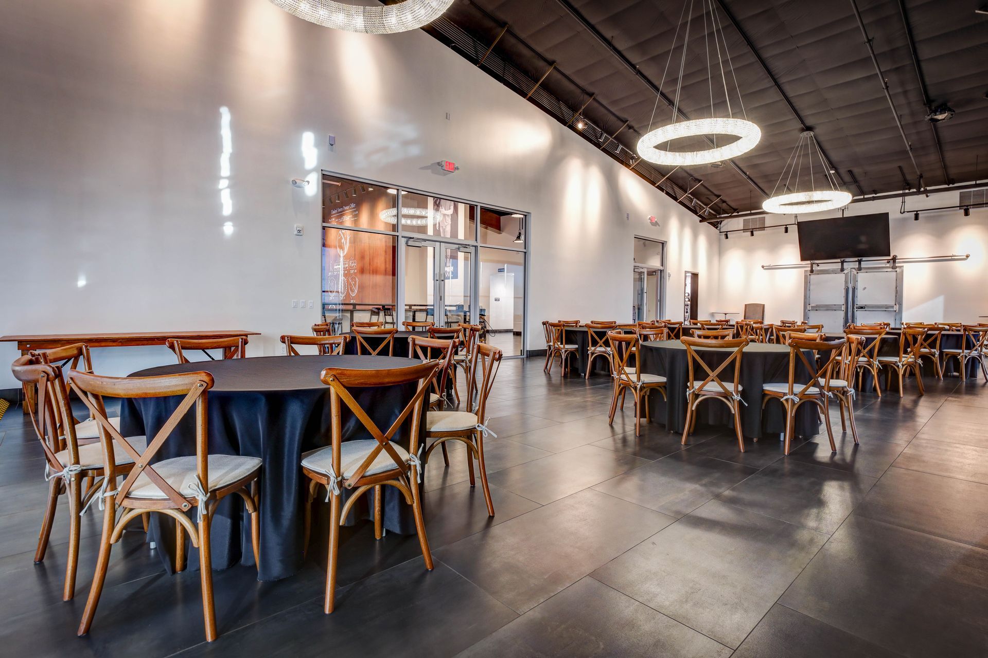 Modern banquet hall with round tables, wooden chairs, and polished dark floors