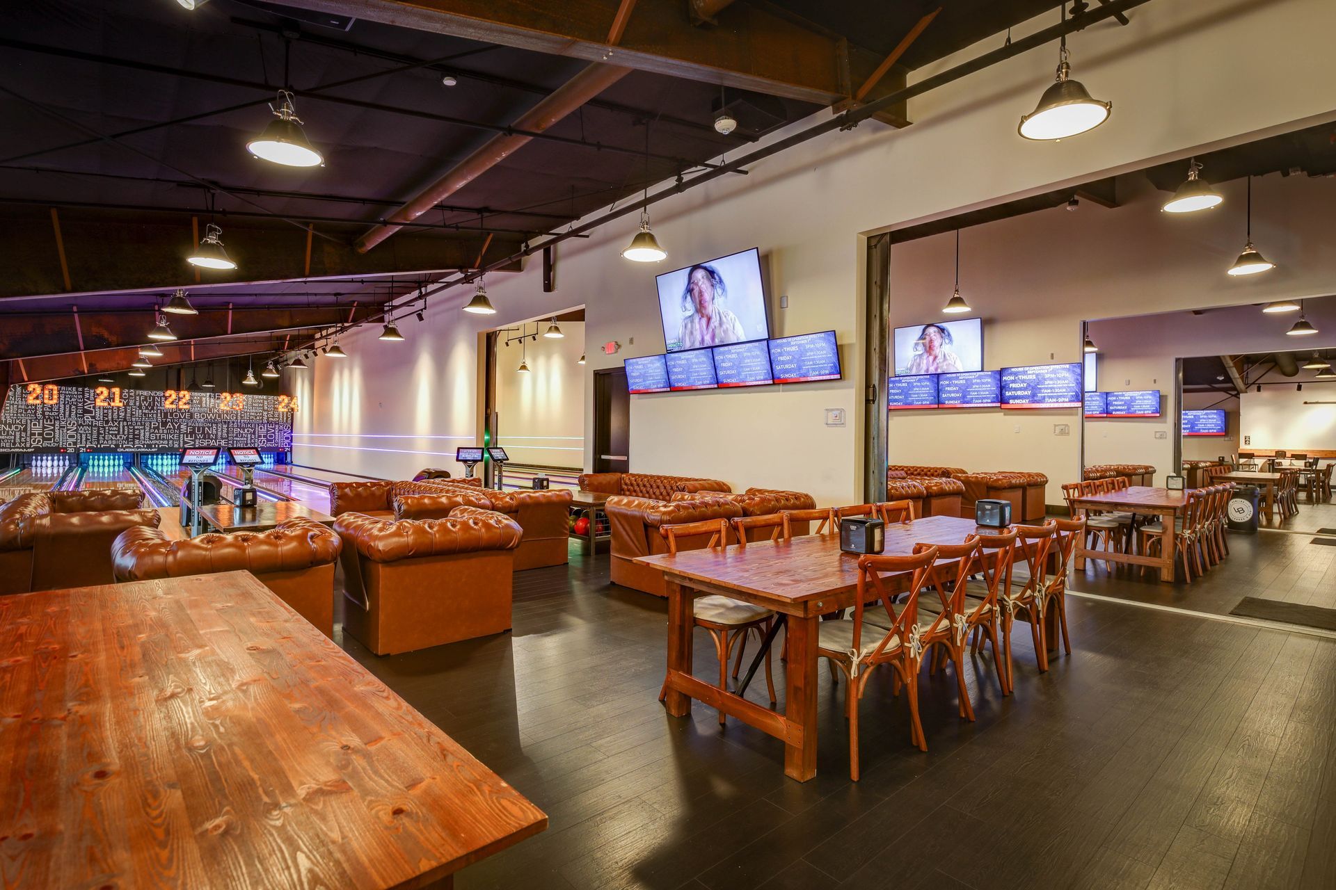 Spacious modern restaurant with wooden tables, orange booths, hanging lights, and TVs on the wall