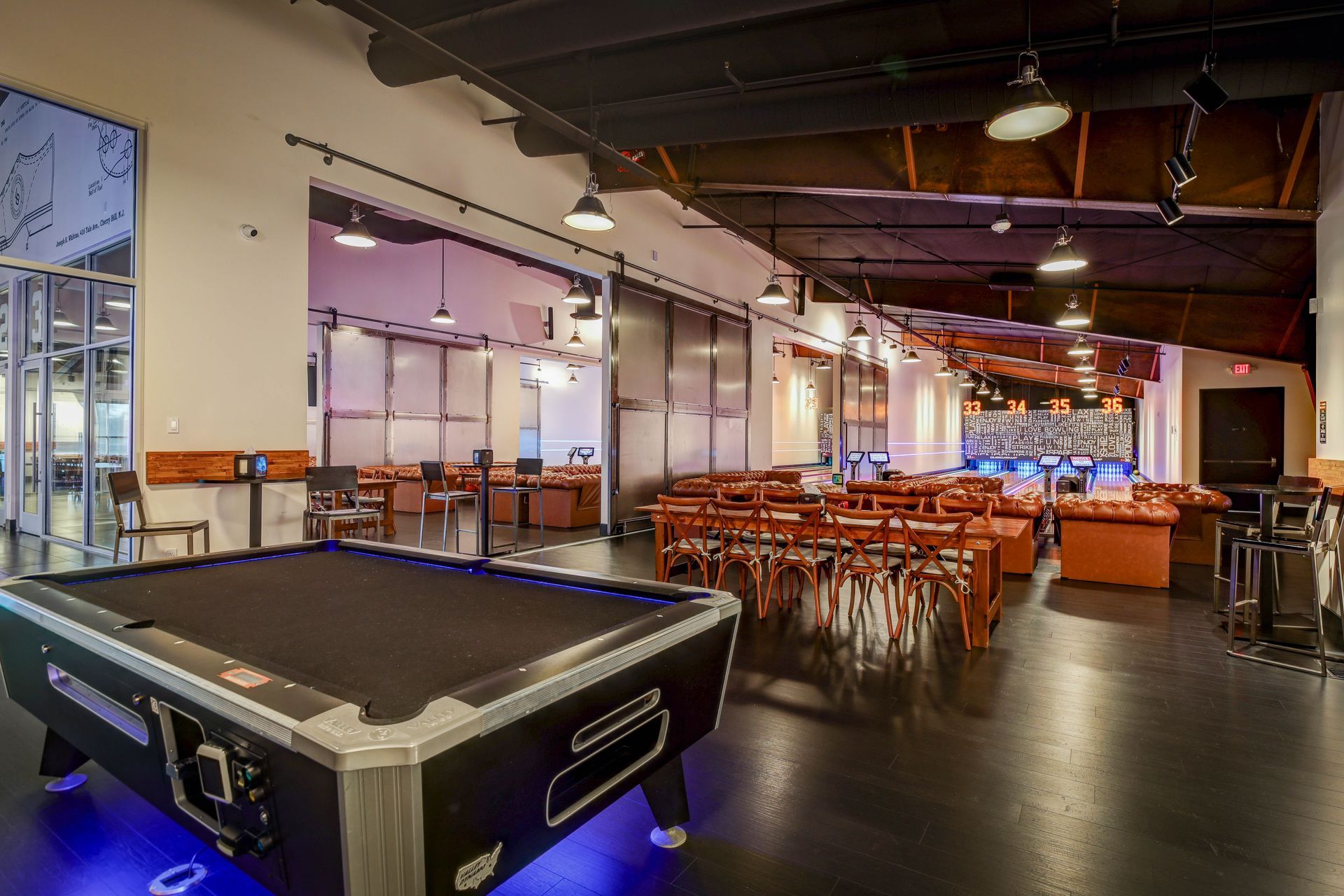 Empty restaurant/bar interior with pool table, orange chairs, and hanging lights