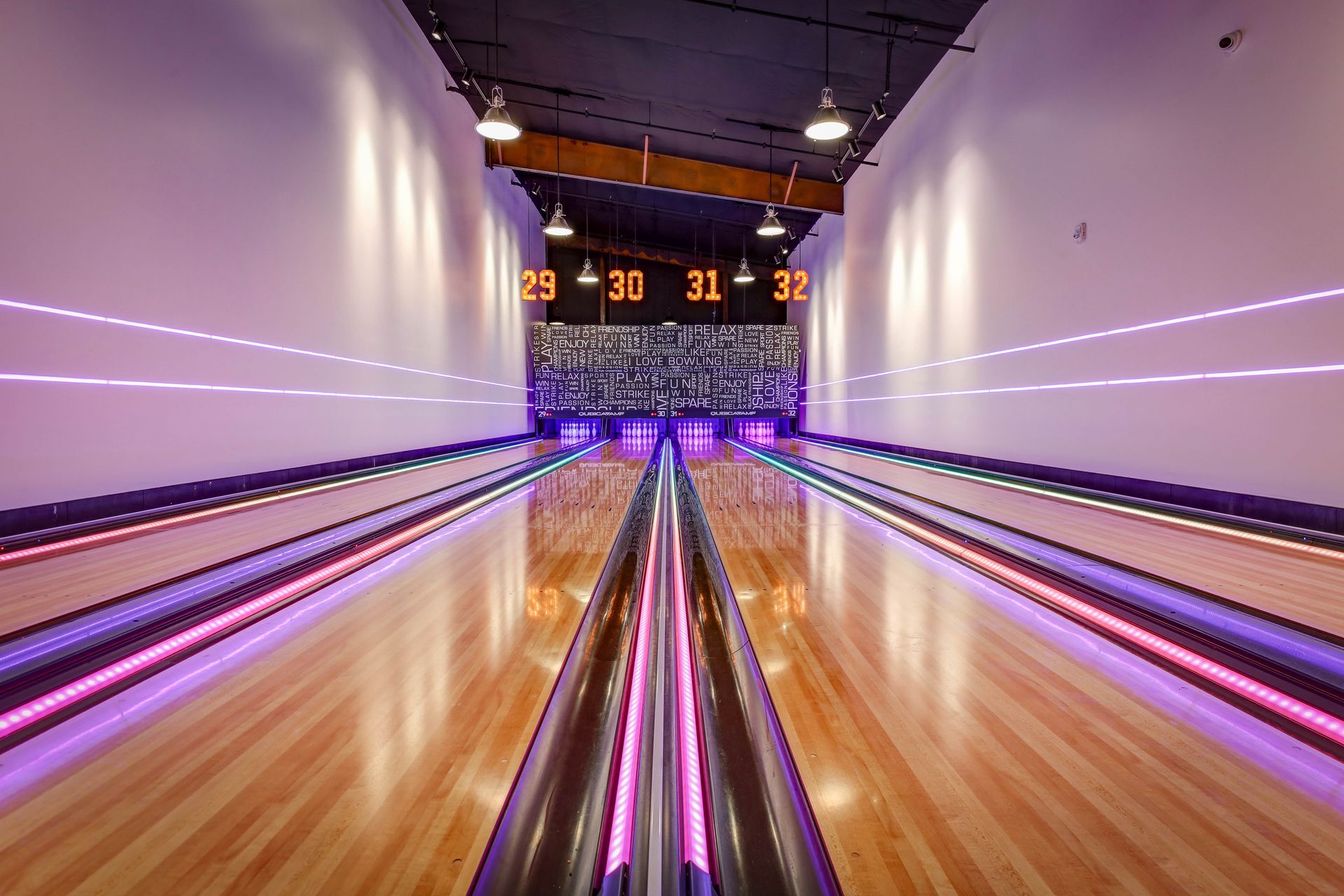 Bowling alley lanes lit in purple and orange, viewed from the foul line toward pins and scoreboards.
