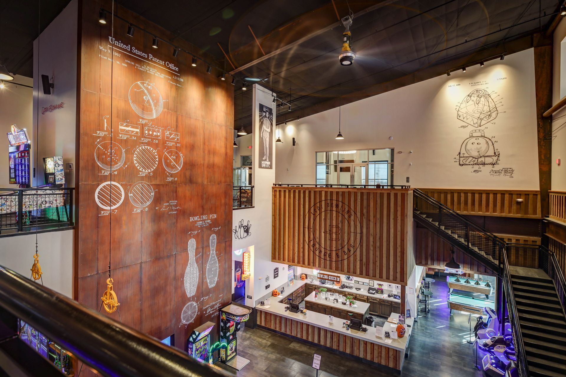 Spacious indoor atrium with hanging lights, tall wood walls, and stairways around a central seating area