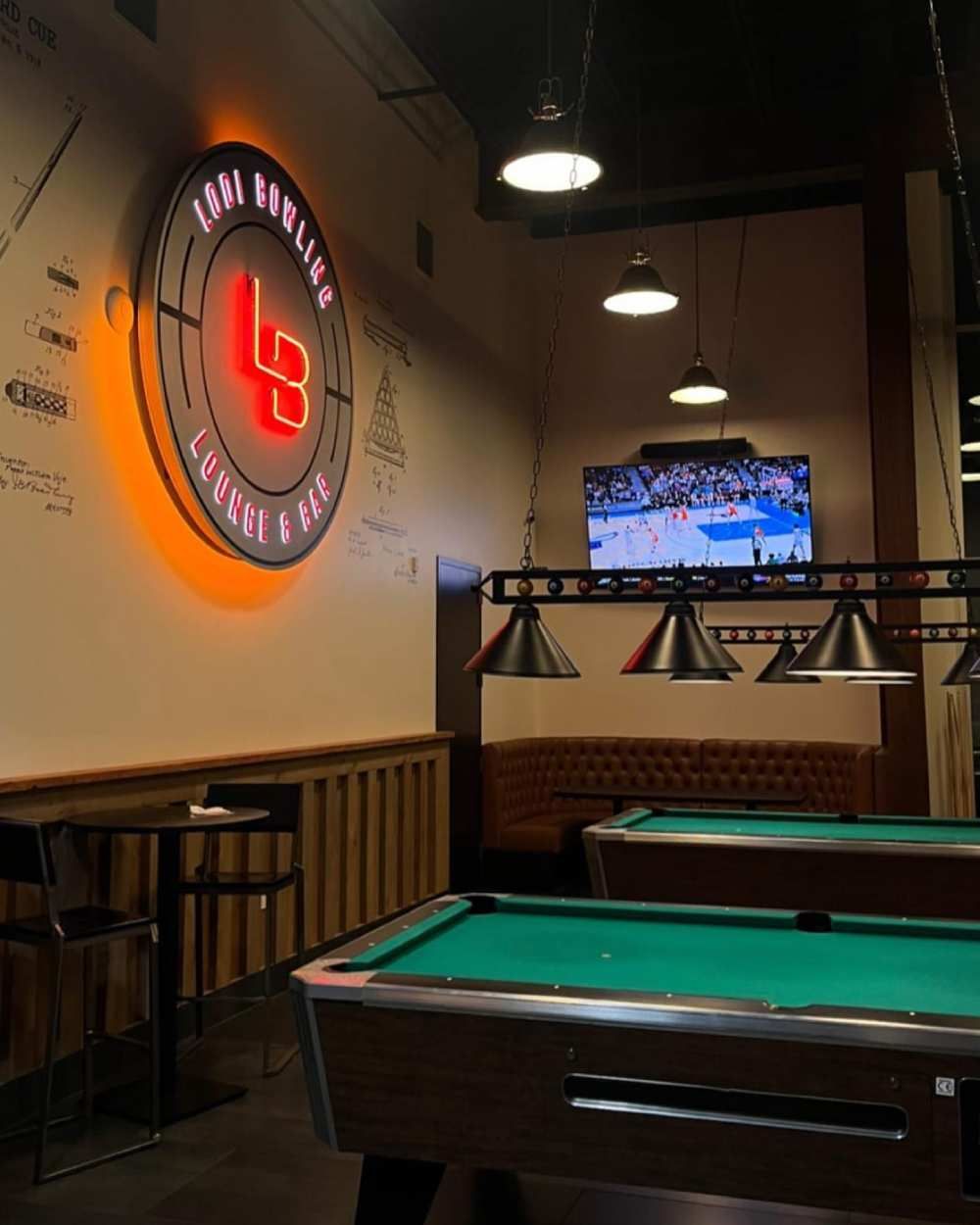 Pool hall with green tables, wall logo, and TV showing a game