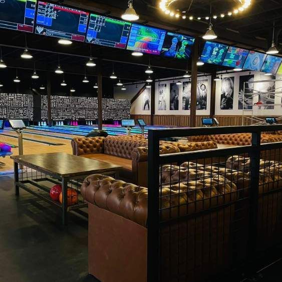 Spacious bowling alley lounge with tufted leather seating, lanes, and colorful overhead monitors.