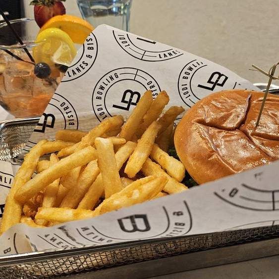 Burger and fries in a basket with branded paper, with a drink and lemon garnish in the background