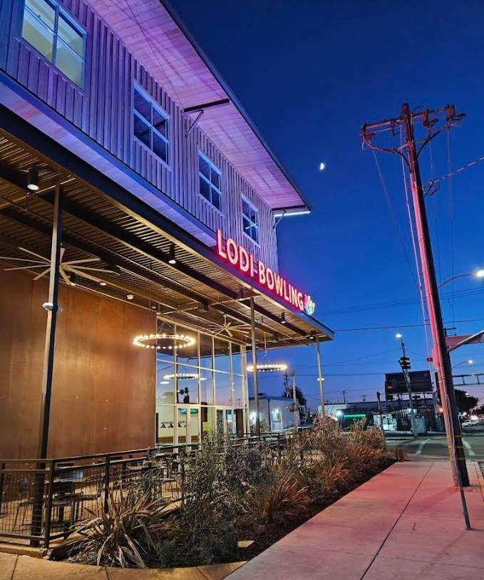 Purple-lit restaurant exterior at dusk with patio seating and a sidewalk along the street