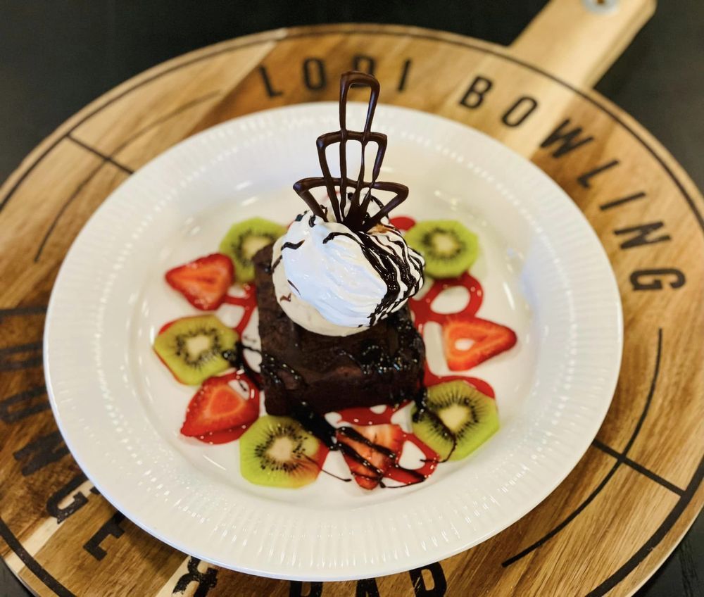 Chocolate dessert with whipped cream and chocolate drizzle, garnished with kiwi and strawberry slices on a white plate