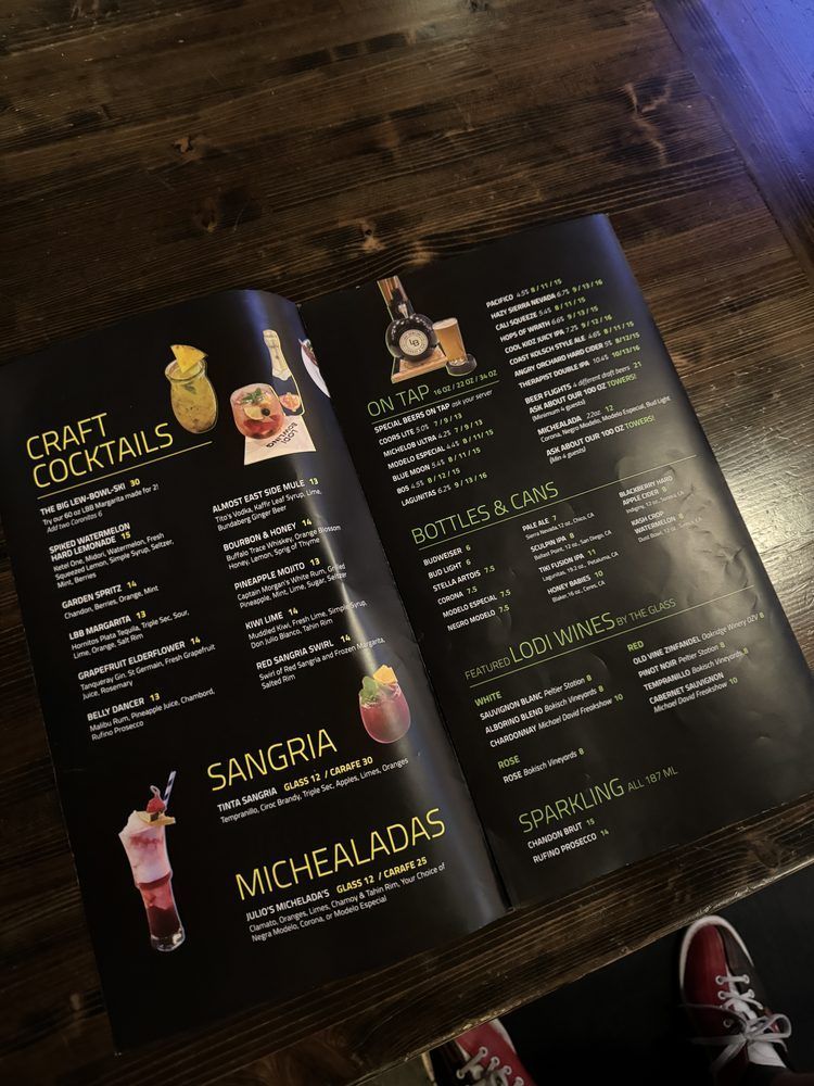 Open cocktail menu on a wooden table, showing colorful drink illustrations and recipe listings.