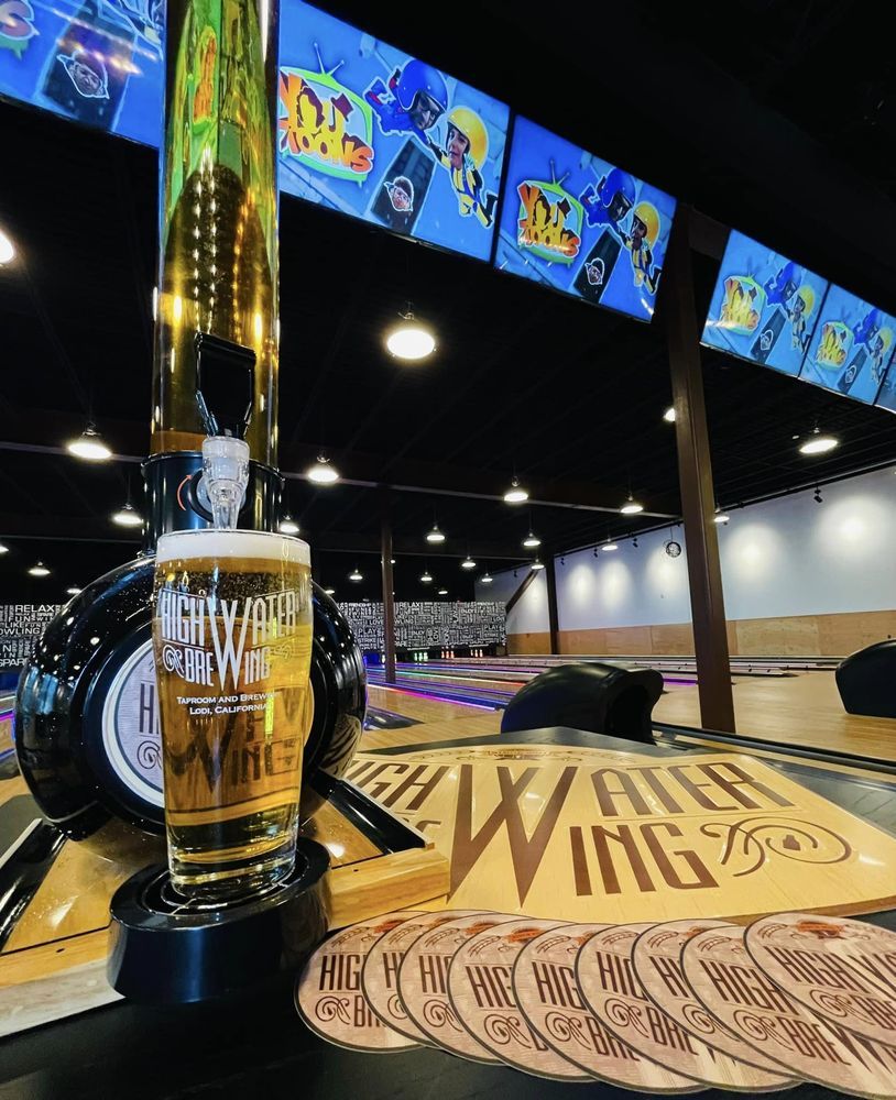 Beer tap and pint on a table at an indoor bowling alley with lanes and overhead screens
