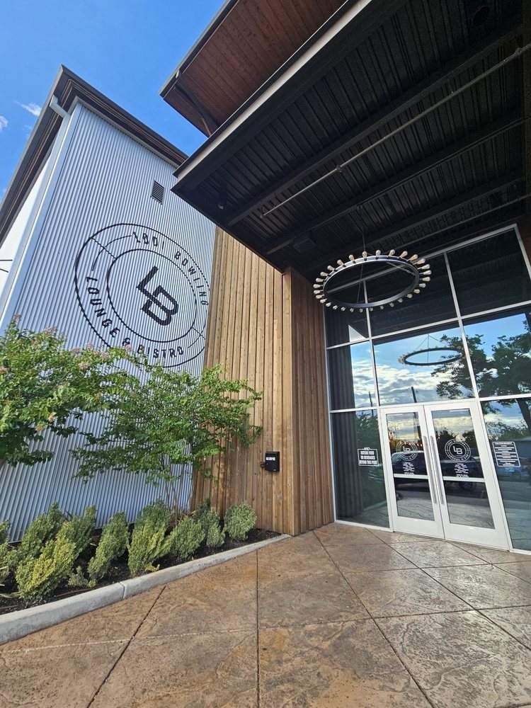 Modern building entrance with glass doors, wood siding, corrugated metal wall, and circular hanging sign.