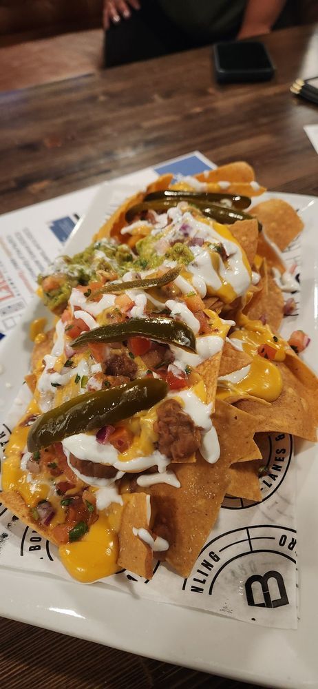 Loaded nachos topped with cheese, jalapeños, drizzled sauces, and diced tomatoes on a tray.