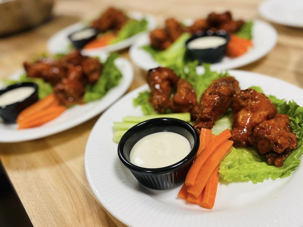 Plates of glazed chicken wings with carrots, celery, and dipping sauce on a table