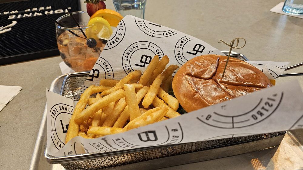 Basket of fries and a cheeseburger on a restaurant table, with a drink and condiment cups in the background.