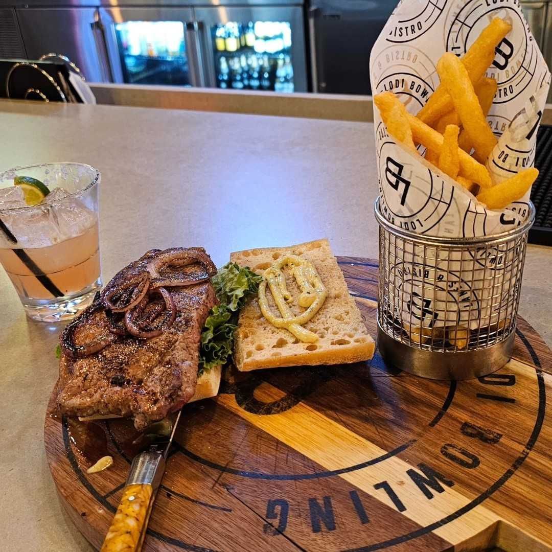 Grilled steak and toast on a wooden board with fries in a paper cup at a restaurant table