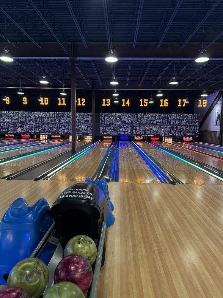 Bowling alley lane with balls in the return rack, aiming toward pins under numbered signs
