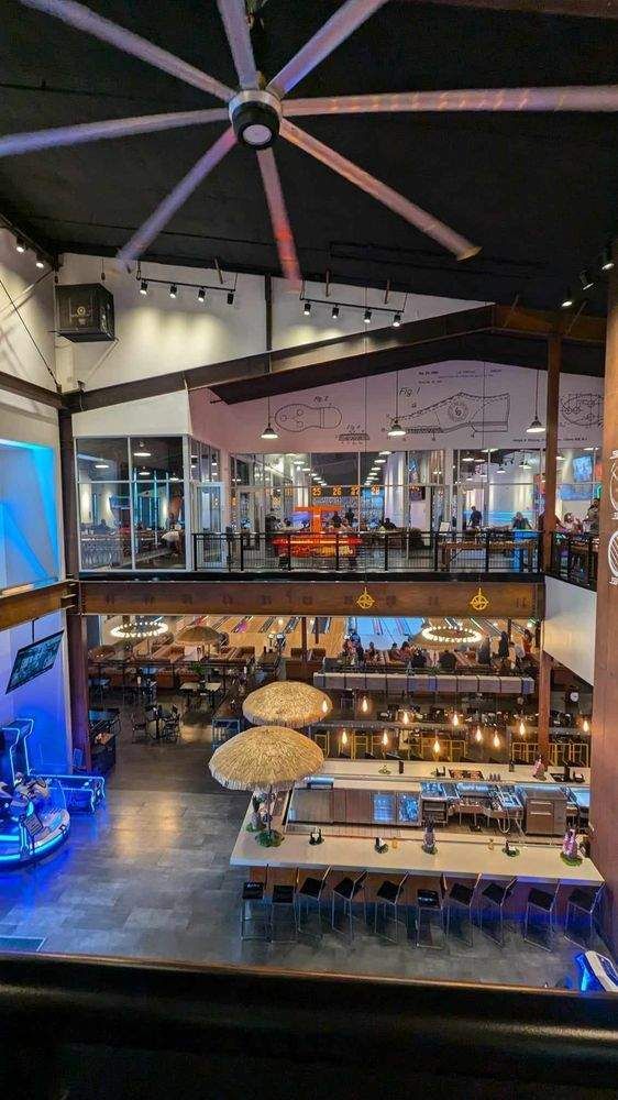 Open-air restaurant interior with upper and lower dining levels, warm lights, and a large ceiling fan